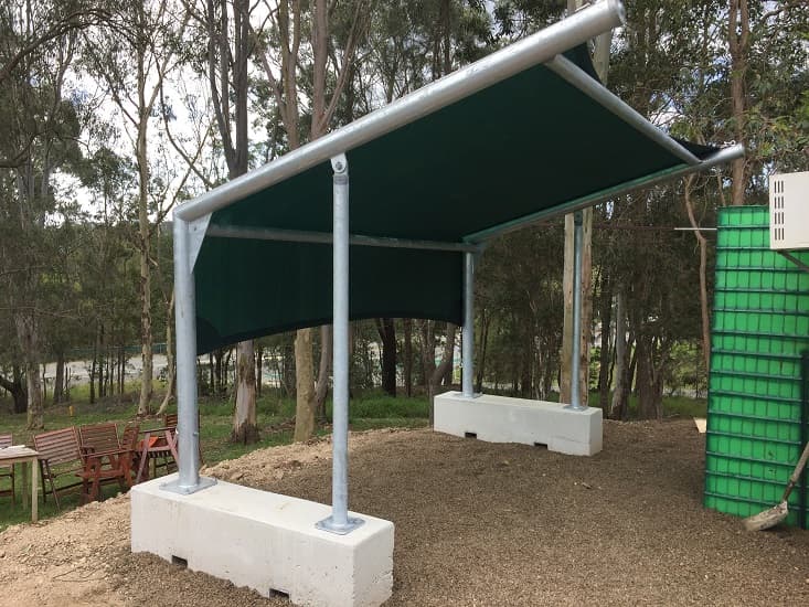 A temporary shade structure, with shade cloth wall, mounted on cement bricks